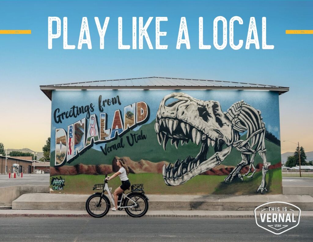 Play like a local in Vernal, Utah. Woman riding her bike in front of the dinoland mural.
